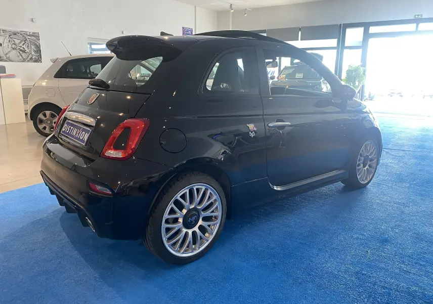 Vue 3/4 arrière droite d'une ABARTH 595 noire avec jantes alu 17 pouces et toit ouvrant électrique en intérieur showroom.
