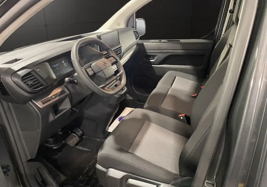 Intérieur du Citroën Jumpy Fourgon 2024 vu côté conducteur, sièges tissu bi-ton gris et tableau de bord moderne.