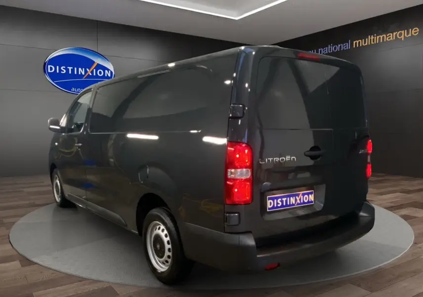 Vue 3/4 arrière droite du Citroën Jumpy Fourgon gris platinium avec feux arrière allumés en showroom.