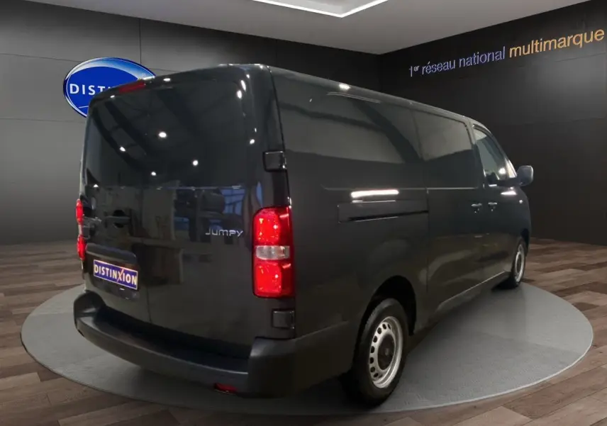 Vue 3/4 arrière droite du Citroën Jumpy Fourgon gris platinium avec feux arrière allumés en intérieur showroom.