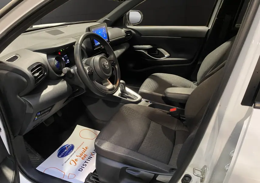 Intérieur noir du Toyota Yaris Cross blanc, vue côté conducteur avec volant cuir et écran tactile central visible.