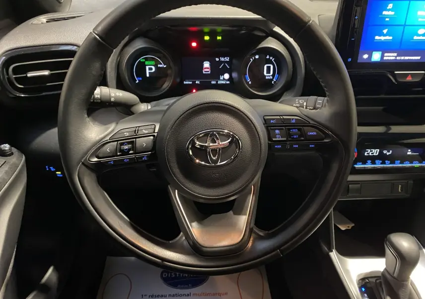 Vue rapprochée du volant en cuir noir et du tableau de bord digital d'une Toyota Yaris Cross blanche 2023 hybride.