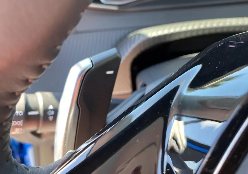 Gros plan sur la palette de changement de vitesses au volant d'un Peugeot 2008 bleu Vertigo, intérieur moderne.