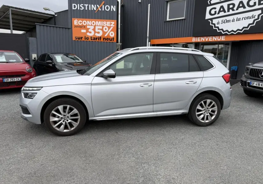 Profil côté gauche d'un Skoda Kamiq gris métallisé 2022 garé devant un garage avec jantes alliage 17 pouces.