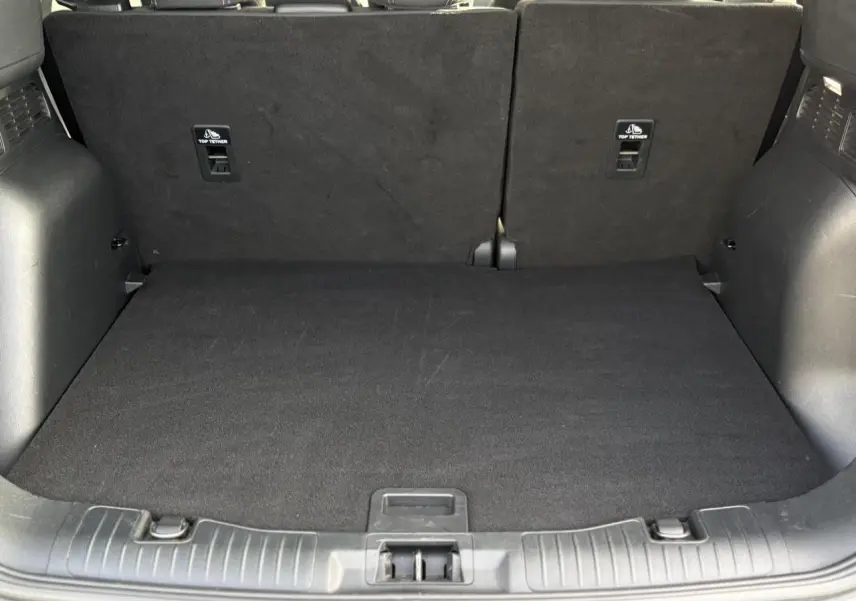 Coffre spacieux du Ford Kuga 2024 vu de face, avec plancher de coffre ajustable et sièges arrière noirs relevés.