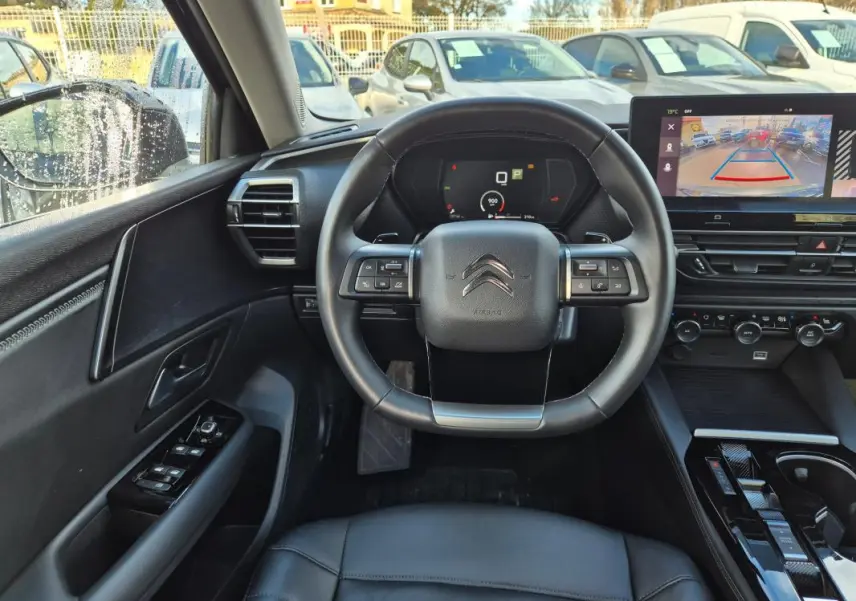 Vue intérieure centrée sur le volant cuir noir et le tableau de bord digital de la Citroën C5 X 2024 avec écran de caméra de recul.