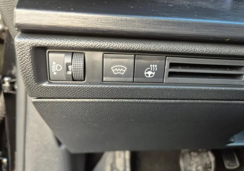 Gros plan sur les commandes noires du tableau de bord côté gauche du Citroën C5 X 2024, avec réglage des phares et chauffage du volant.