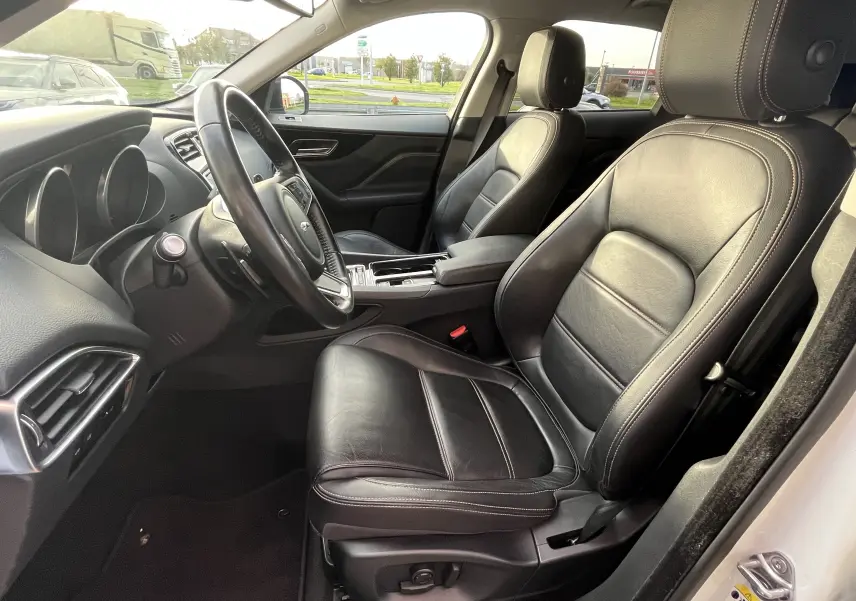 Intérieur avant droit du Jaguar F-PACE blanc 2018, sièges cuir noir chauffants et tableau de bord moderne.