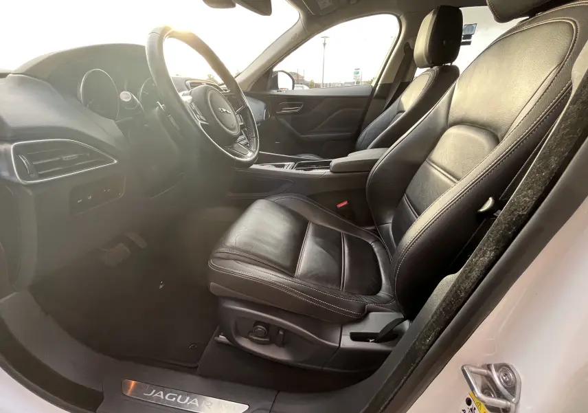 Vue intérieure côté gauche du Jaguar F-PACE blanc 2018, mettant en valeur les sièges en cuir noir et le volant multifonction.
