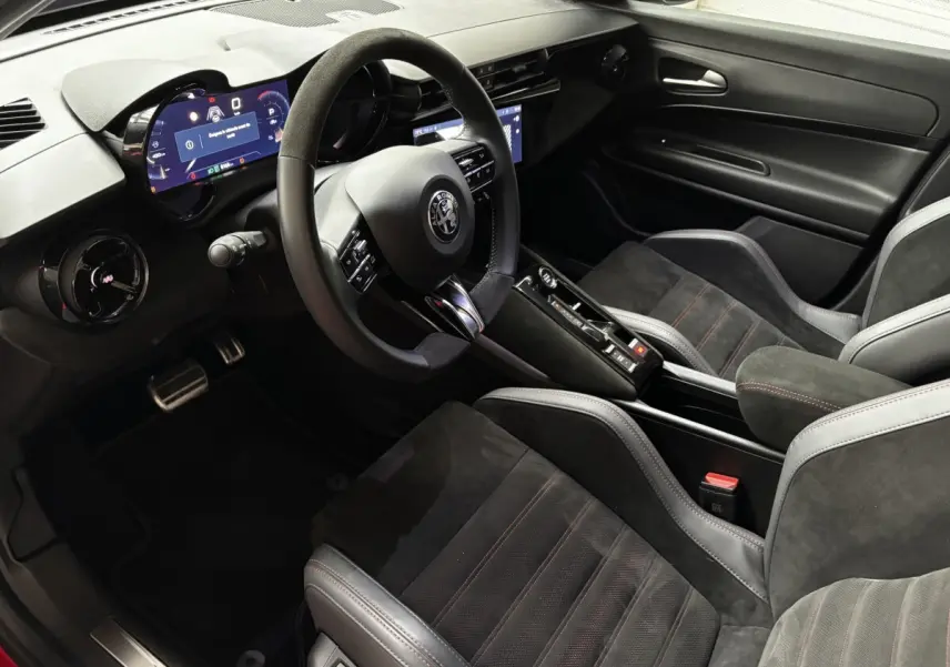 Vue intérieure côté conducteur de l'Alfa Romeo Junior 2024, sièges Sabelt noirs avec surpiqûres rouges et tableau de bord digital.