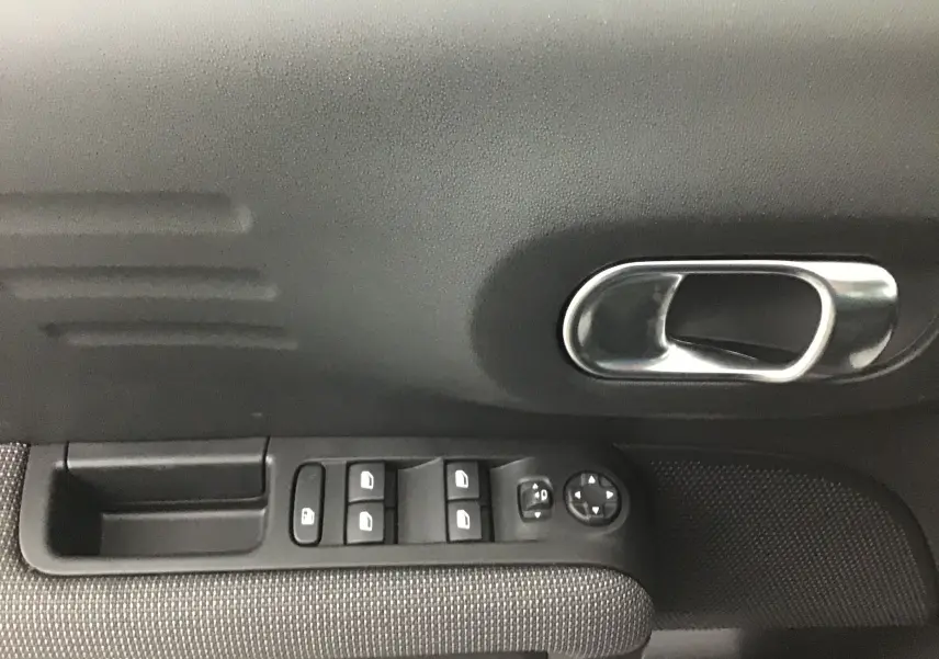 Poignée intérieure côté gauche avec commandes des vitres et rétroviseurs du Citroën C3 Aircross noir 2024.