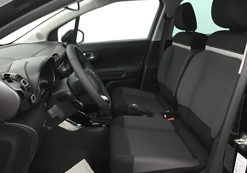 Vue intérieure côté conducteur de la Citroën C3 Aircross 2024, sièges tissu noir et tableau de bord moderne.