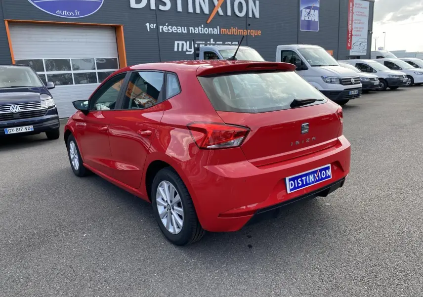 Vue 3/4 arrière gauche d'une SEAT Ibiza rouge pur 2021 avec jantes alliage 15 pouces, stationnée devant un concessionnaire multimarque.