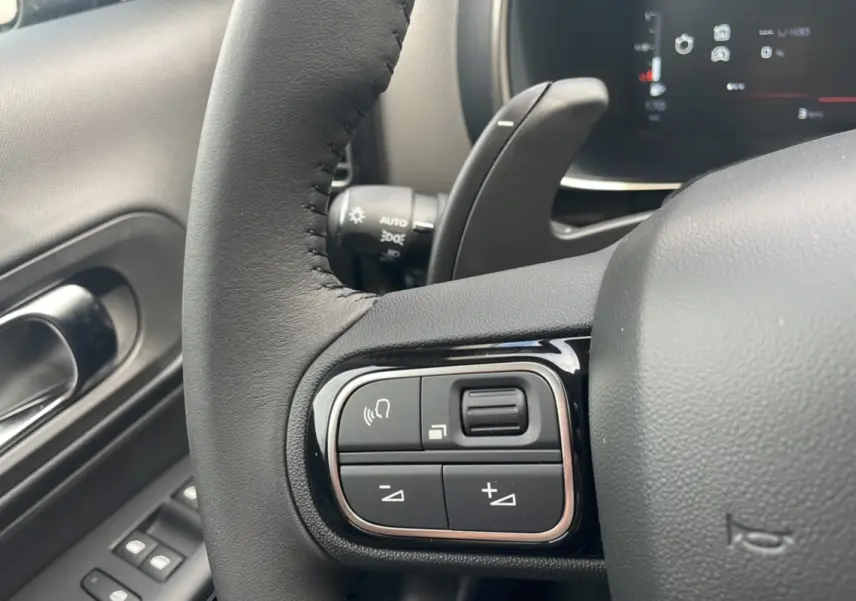 Gros plan sur les commandes au volant du Citroën C5 Aircross Hybrid 2025, intérieur noir avec détails chromés.