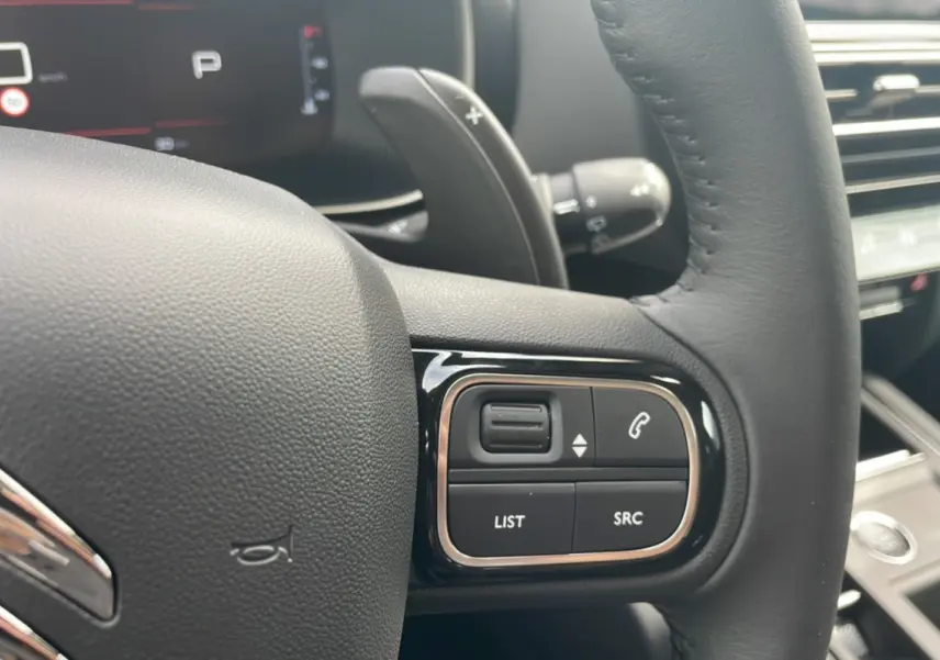 Gros plan sur les commandes du volant cuir noir du Citroën C5 Aircross Hybrid 2025, affichage numérique en arrière-plan.