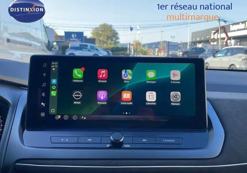 Écran tactile central du Nissan Qashqai 2025 affichant les applications Apple CarPlay, avec vue extérieure floutée.