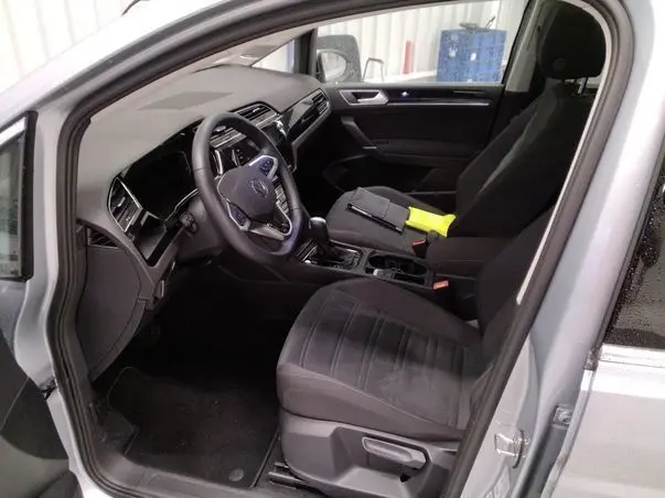Vue intérieure côté conducteur du Volkswagen Touran gris 2025, avec volant multifonctions et sièges tissu noirs.