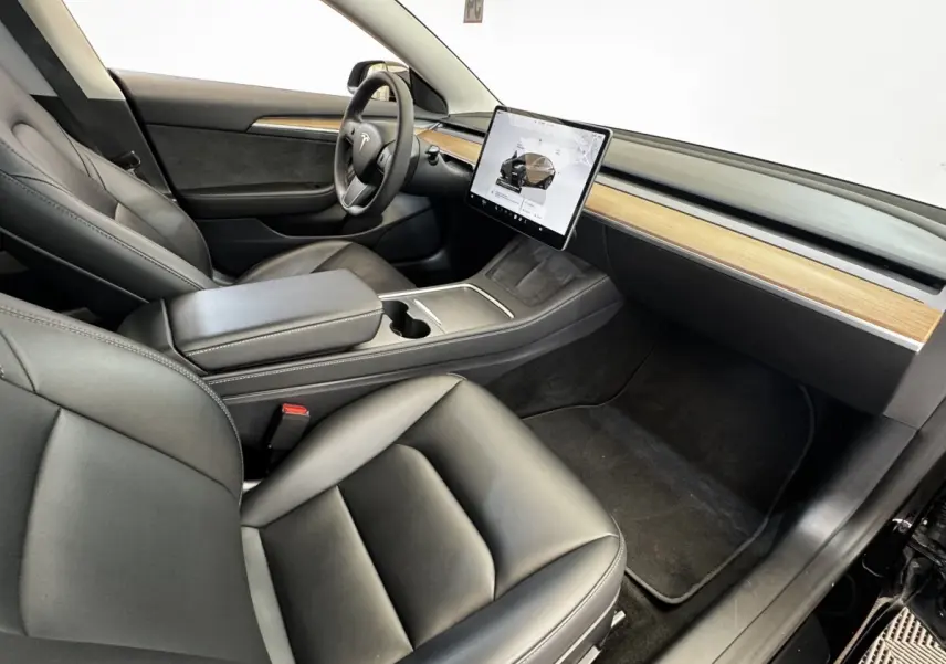 Intérieur Tesla Model 3 noir 2023 vu côté passager, avec écran tactile central et tableau de bord bois clair.