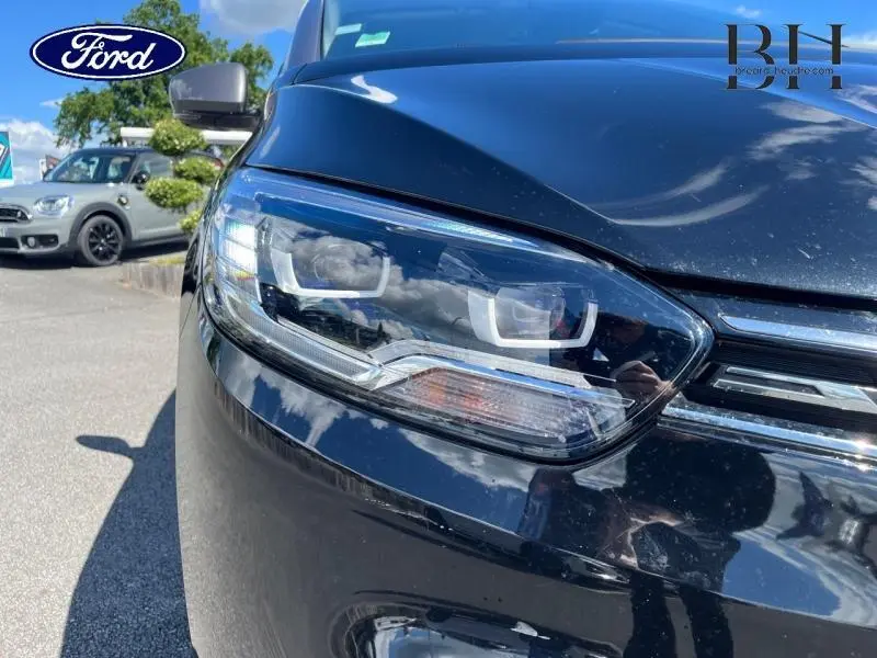 Gros plan sur le phare avant droit du Renault Grand Scenic noir étoilé 2021, reflétant le ciel et les environs.