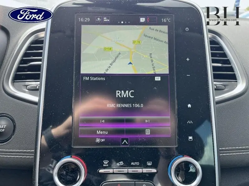 Vue rapprochée de l’écran tactile central du tableau de bord d’un Renault Grand Scenic noir étoilé, affichant la navigation et la radio RMC.