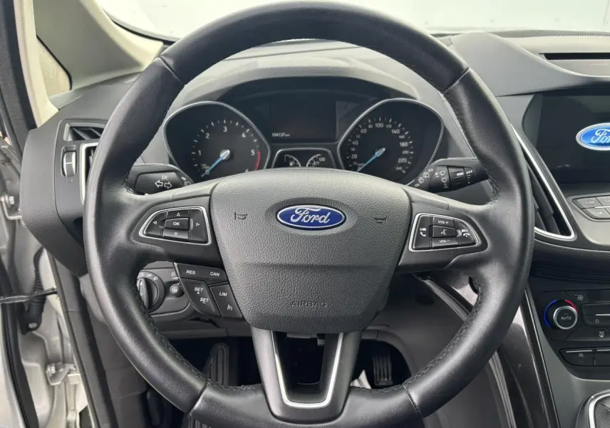Vue rapprochée du volant cuir noir de la Ford C-MAX II avec tableau de bord et écran tactile visible à droite.