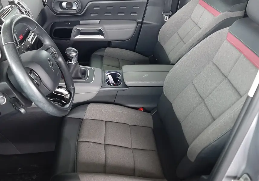 Vue intérieure côté conducteur du Citroën C5 Aircross 2021, sièges gris tissu avec bande rouge et volant cuir noir.