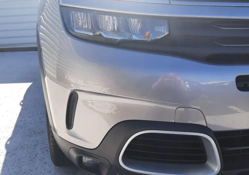 Gros plan sur l'avant gauche du Citroën C5 Aircross gris Artense avec toit noir, mettant en valeur les phares LED et la calandre.