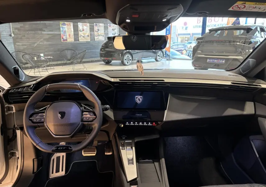 Vue intérieure frontale du poste de conduite de la Peugeot 308 Hybrid blanche avec volant GT et écran tactile central.