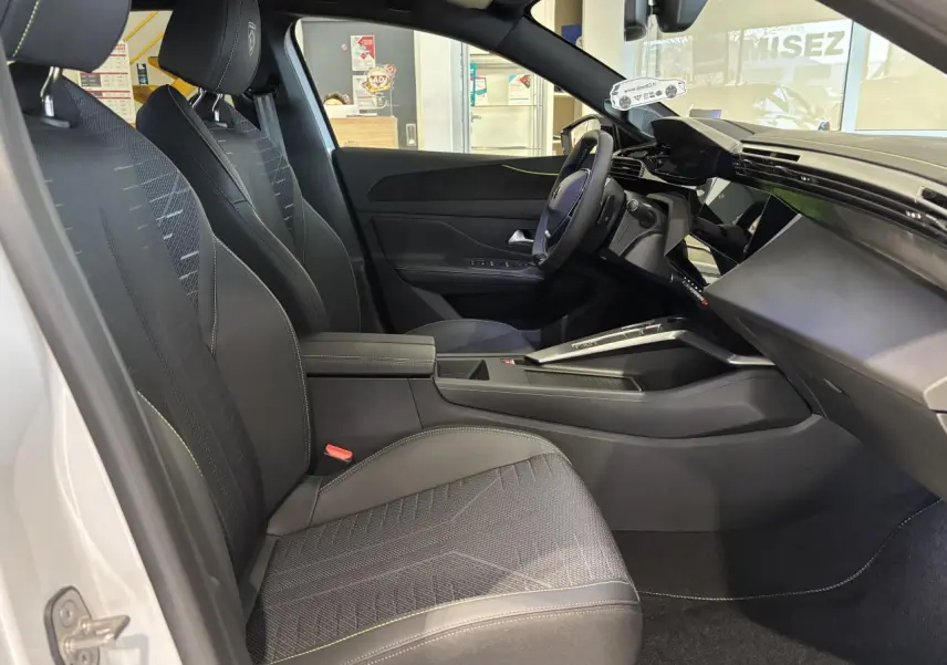 Vue intérieure côté conducteur du Peugeot 308 blanc Okenite 2026, avec sièges noirs et surpiqûres vert Adamite.