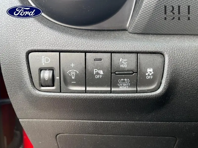 Gros plan sur les commandes noires du tableau de bord du Hyundai Kona Pulse Red Métal, avec réglage phares et assistance conduite.