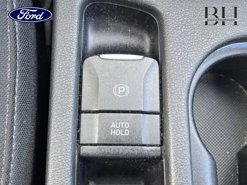 Gros plan sur la console centrale montrant le bouton de frein de parking électronique et la fonction Auto Hold, intérieur noir.