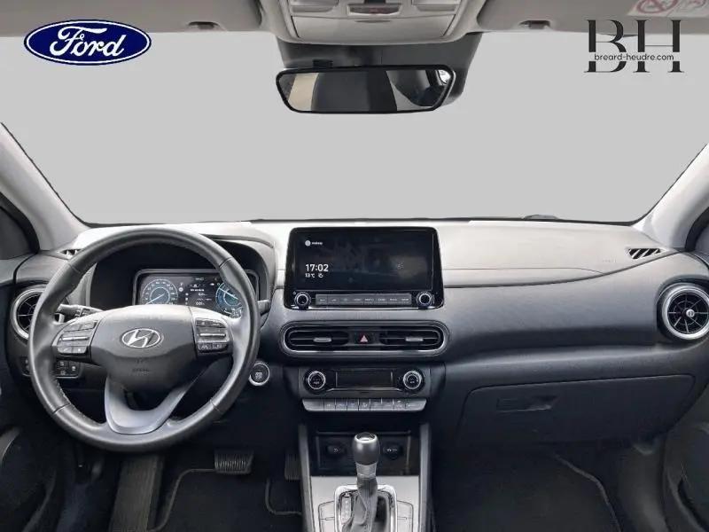 Vue frontale de l'habitacle du Hyundai Kona rouge, avec tableau de bord noir et écran tactile central.
