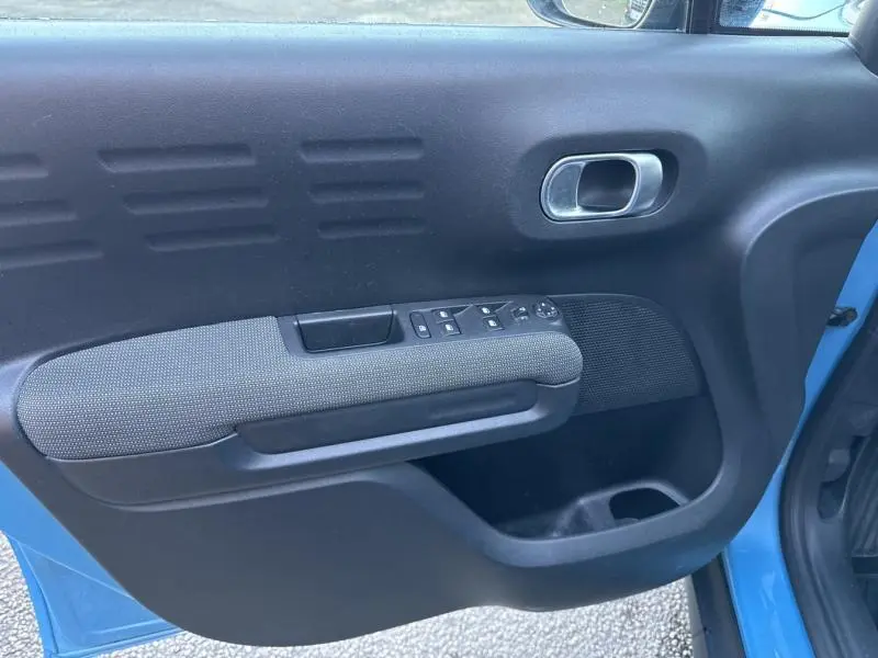 Vue rapprochée de la porte avant gauche bleu Breathing Blue d'une Citroën C3 Aircross avec accoudoir tissu gris et commandes électriques.