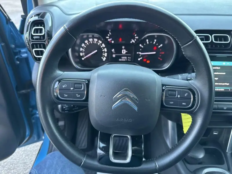 Vue centrée sur le volant cuir noir du Citroën C3 Aircross Breathing Blue avec tableau de bord et portière ouverte côté gauche visible.