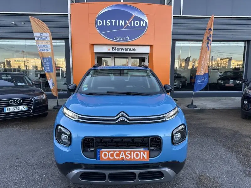 Vue frontale d'un Citroën C3 Aircross bleu Breathing avec barres de toit et plaque "OCCASION" visible.