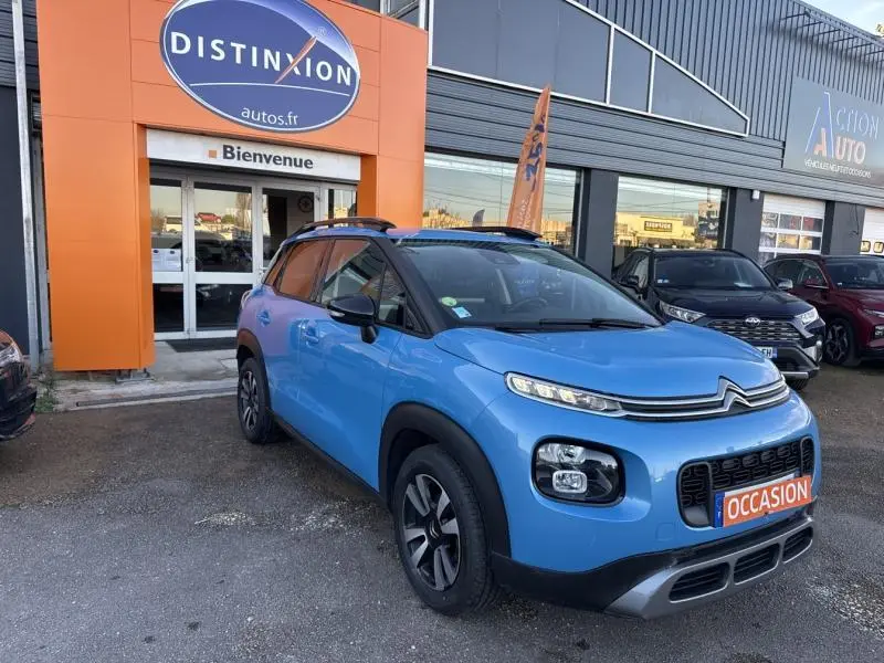 Vue 3/4 avant gauche d'un Citroën C3 Aircross bleu Breathing avec barres de toit et jantes alliage.