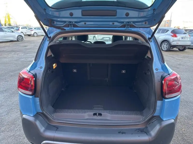 Coffre ouvert vu de l'arrière d'un Citroën C3 Aircross bleu Breathing Blue avec hayon relevé et banquette arrière visible.