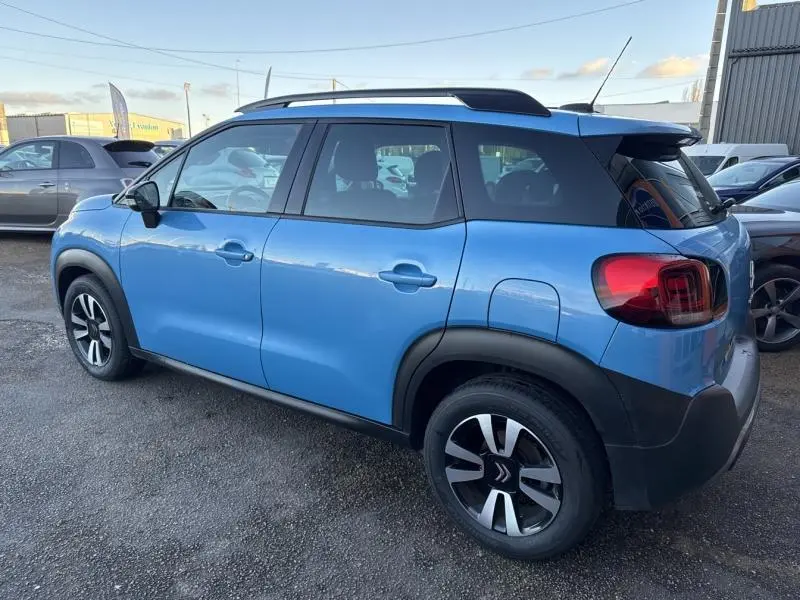 Vue 3/4 arrière côté gauche d'un Citroën C3 Aircross bleu Breathing avec barres de toit et jantes alliage.