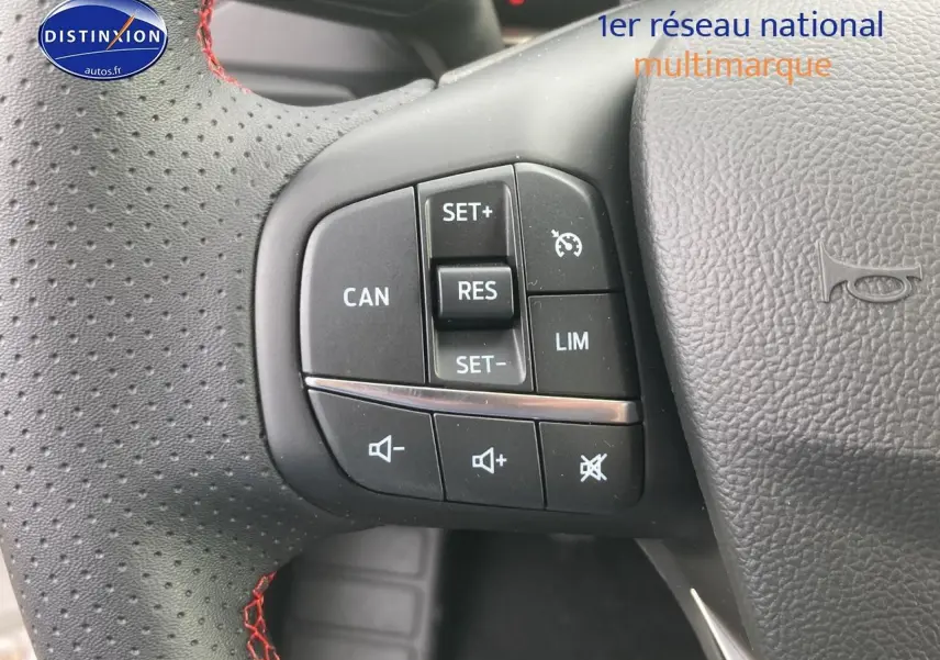 Gros plan sur le volant perforé noir avec coutures rouges et commandes de régulateur de vitesse de la Ford Focus gris 2025.