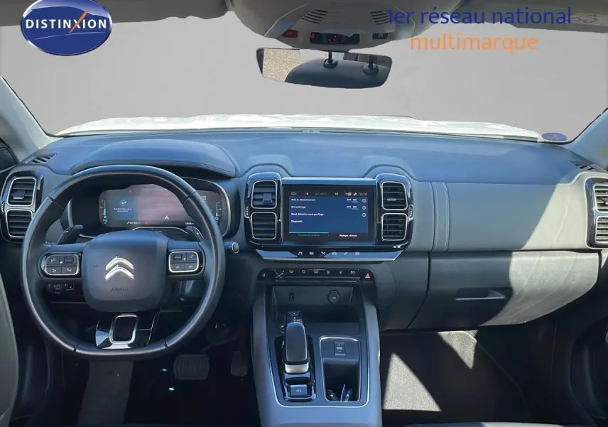 Vue intérieure du tableau de bord et volant noir du Citroën C5 Aircross blanc nacré hybride, avec écran tactile central allumé.