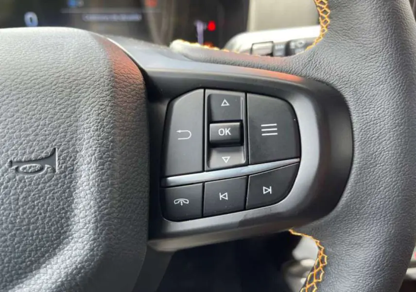 Gros plan sur les commandes multifonctions à droite du volant noir avec surpiqûres orange du Ford Ranger Wildtrak Plus 2025.