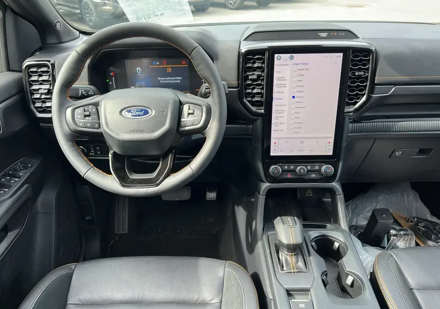 Vue intérieure frontale du tableau de bord du Ford Ranger 2025, volant cuir noir avec surpiqûres jaunes et écran tactile vertical.