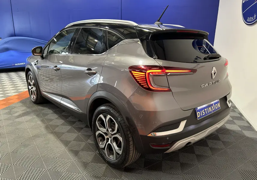 Vue 3/4 arrière droite d’un Renault Captur gris avec feux LED allumés et toit noir dans un showroom.