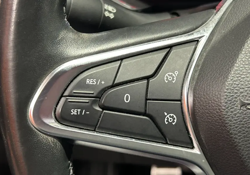 Gros plan sur les commandes de régulateur de vitesse au volant noir du Renault Captur gris 2020.