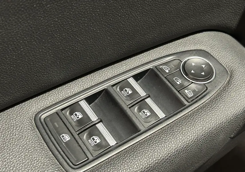 Gros plan sur les commandes des vitres électriques et rétroviseurs sur la porte côté conducteur d’un Renault Captur gris.