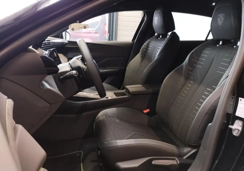Intérieur avant droit de la Peugeot 308 GT 2026 noir métallisé, sièges tissu noir avec surpiqûres vert Adamite.