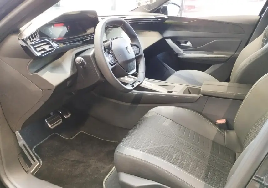 Vue intérieure côté conducteur de la Peugeot 308 1.2i Hybrid 2026, avec sièges noirs et volant compact GT cuir.