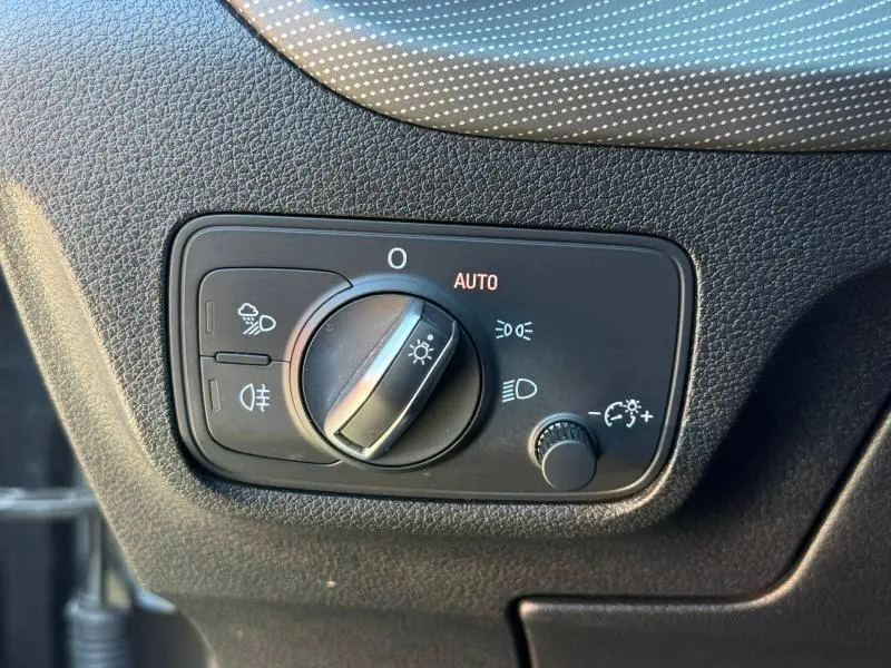Gros plan sur le sélecteur de phares intérieur de l'Audi Q2 35 TDI 150ch S line 2025, avec finition noire texturée.
