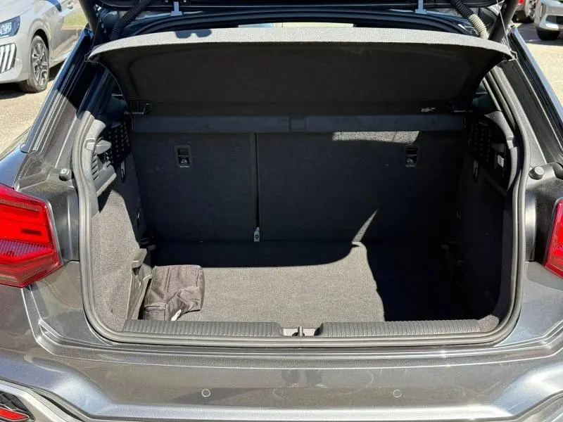 Coffre ouvert vu de l'arrière d'un Audi Q2 35 TDI S line gris Daytona nacré avec intérieur de coffre vide et tapis noir.