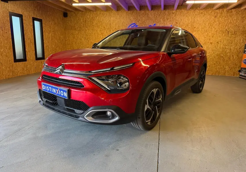 Citroën C4 X rouge vue 3/4 avant droit dans un garage avec éclairage intérieur et jantes noires.